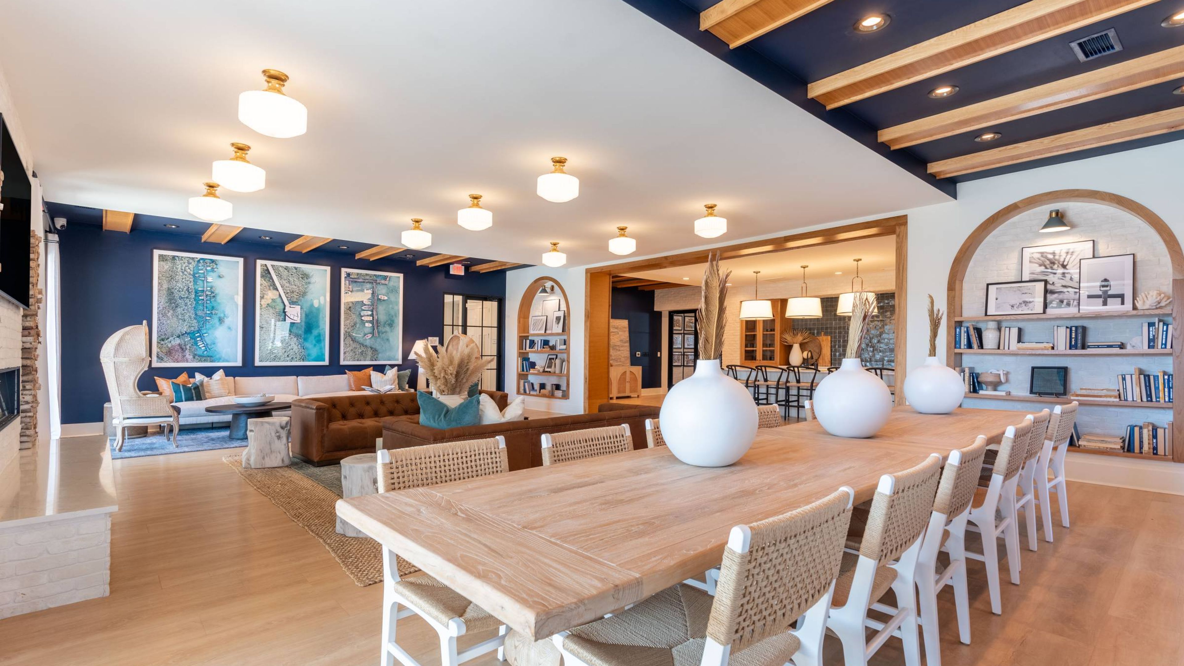 Hawthorne Cottages at Leland  lounge featuring a comfortable sofa, wicker chair, and three large aerial photographs of a marina on a dark blue accent wall.