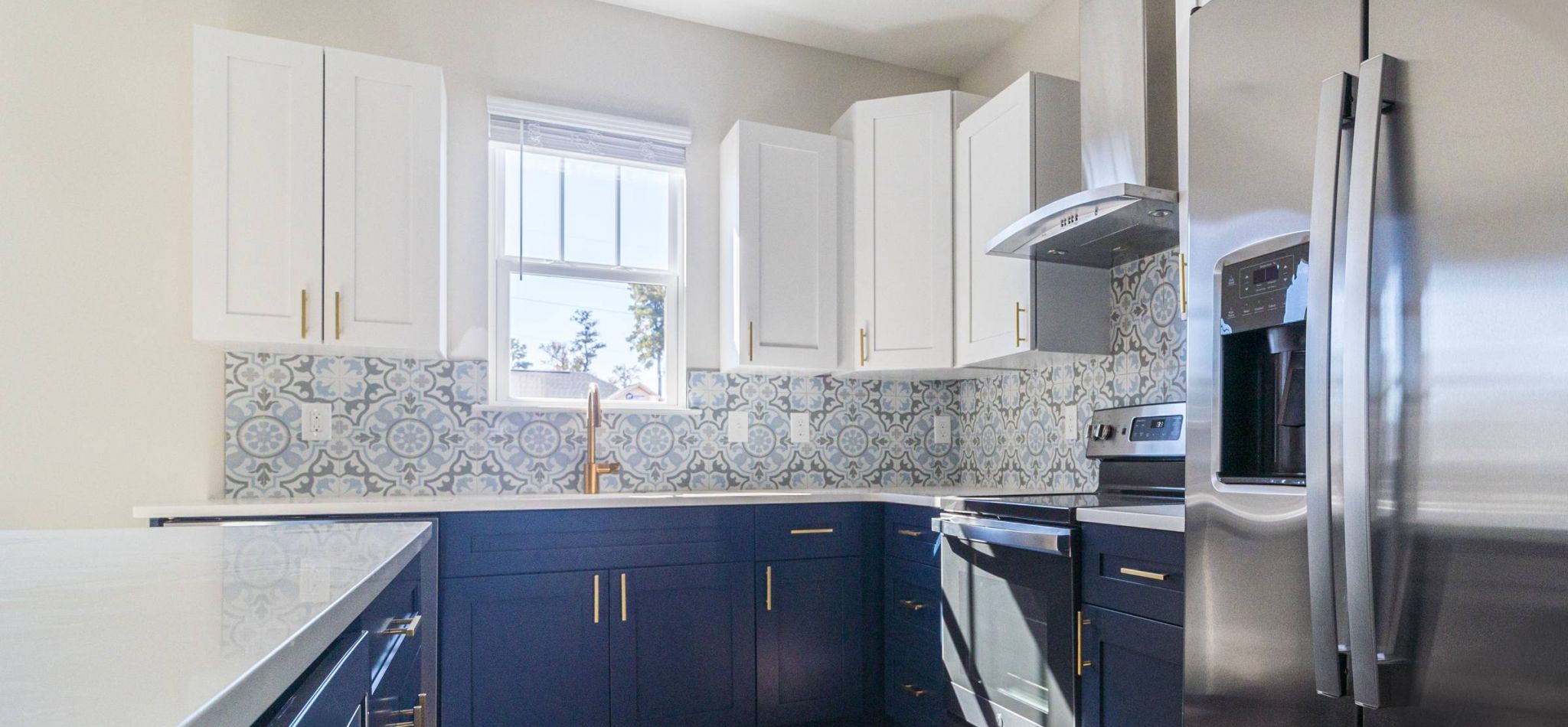 Hawthorne Cottages at Leland modern kitchen featuring white upper cabinets, navy blue lower cabinets, patterned backsplash, and stainless steel appliances.
